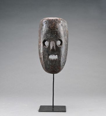un masque en bois posé sur un socle, devant un fond gris