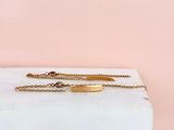 a gold plated bracelet on a marble block with a pink background