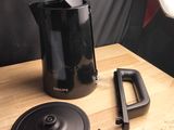 une cafetière noire posée sur une table en bois, avec une télécommande