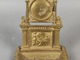 une horloge dorée posée sur un socle, sur une surface blanche