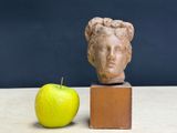 a statue of a woman ' s head next to a green apple