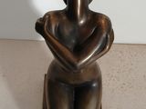 statue d'une femme assise sur un socle en bois, les mains posées sur les genoux
