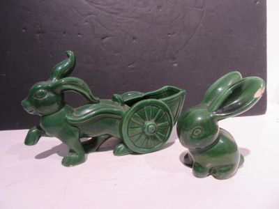 deux statues vertes représentant des lapins tirant une charrette sur laquelle se trouve un lapin