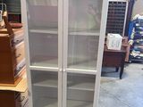 a tall white cabinet with glass doors in a warehouse