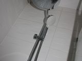 a shower head in the corner of a white tiled bathroom
