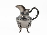 a silver pitcher that is on a stand on a white surface