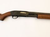 un fusil de chasse posé sur une surface blanche, muni d'une crosse en bois