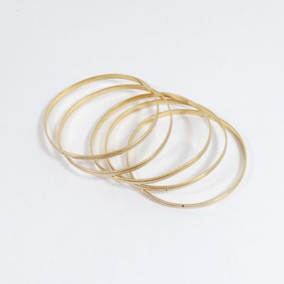 une pile de bracelets « bangies » dorés sur fond blanc