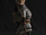 une statue en bois représentant un homme portant un sac à dos sur le dos