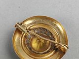 gold plated cup and saucer with a gold broocher in the center