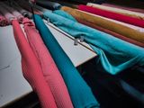 many different colored fabrics hanging on a rack in a room