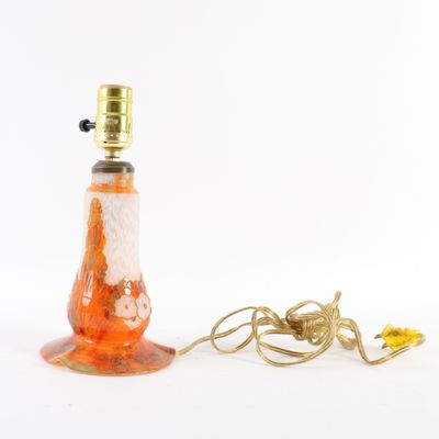 une lampe en verre orange et blanc, avec un pied en métal doré et un cordon