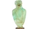 une image représentant un vase en verre vert posé sur un socle en bois