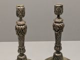 deux bougeoirs en argent posés sur une table blanche, sur fond gris