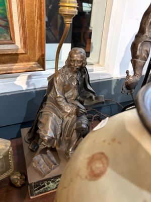 une statue représentant un homme assis sur une chaise à côté d'une lampe