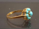 a gold ring with turquoise beads on it on a black surface