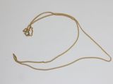 gros plan d'un collier en or avec une chaîne sur une surface blanche