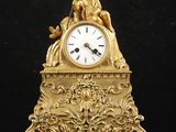 une horloge en or richement décorée posée sur une table noire