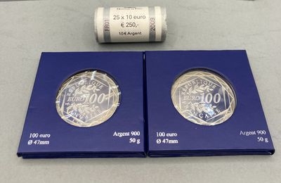 deux pièces d'argent dans une boîte bleue, avec un rouleau de billets en arrière-plan