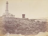 une photo en noir et blanc d'un phare sur un rivage rocheux