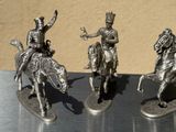 three silver figurines of men riding on horses on a table