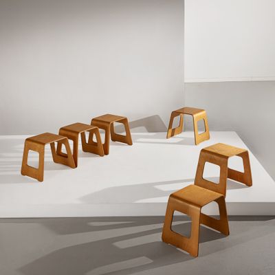 Plusieurs tabourets en bois sont alignés sur une surface blanche