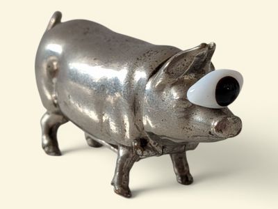 a small metal pig with big eyes on a white surface