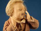 a doll of a boy with blonde hair wearing a brown coat
