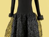 une robe noire posée sur un présentoir à mannequin, sur fond jaune