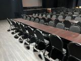 tables and chairs in a conference room with a projector screen in the background