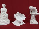 three white figurines of a woman and a man sitting on a rock