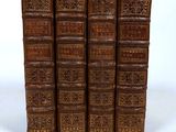 six old books are lined up in a row on a white surface