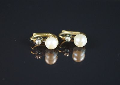 a pair of pearl and diamond earrings on a black surface