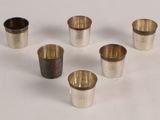 six silver cups are arranged in a circle on a white surface