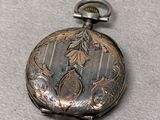 a silver pocket watch with a bird design on it