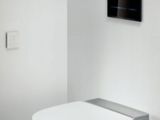 a white toilet sitting in a bathroom with a tv mounted on the wall