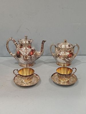 three silver teapots and a cup on a table