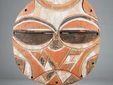 a close up of a wooden mask on a stand on a white surface