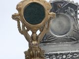 a silver and green clock on a stand next to a mirror