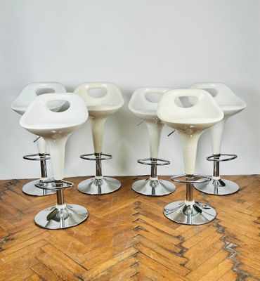 quatre tabourets blancs posés sur un parquet, près d'un mur blanc