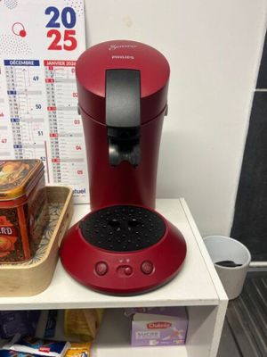 a red coffee maker sitting on a shelf next to a cup of coffee