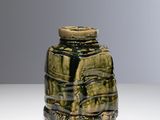 un vase vert posé sur une table, sur fond gris