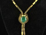 a gold necklace with a green stone pendant on a black mannequin