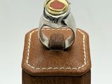 silver and gold ring with a red stone on top of a brown leather box