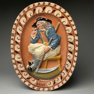 une photo d'une assiette décorative sur laquelle figure un homme assis sur un tabouret