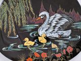 a black plate with a painting of a swan and ducklings on it