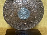 une plaque en bronze ornée d'un motif, posée sur un socle noir
