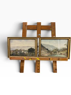 two paintings are hanging on a wooden easel on a white wall