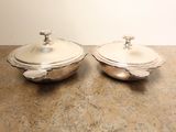 two silver dishes on a table with a white wall in the background