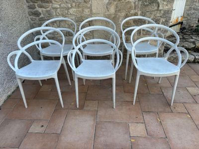 six chaises blanches disposées devant un mur de pierre